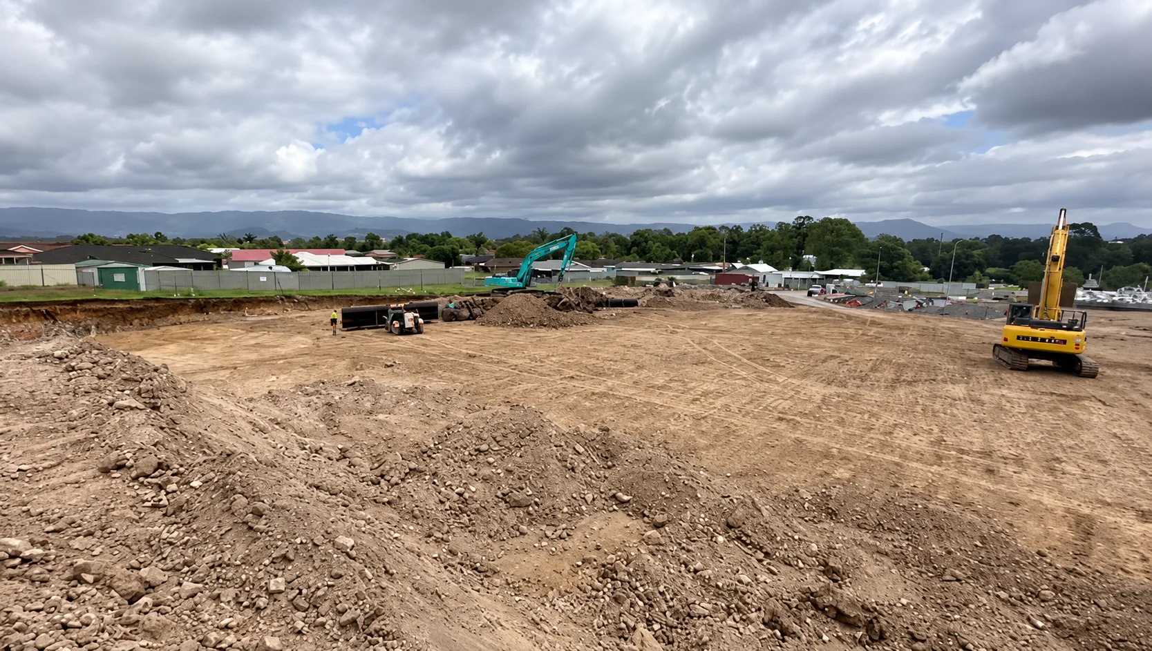 An open excavation site with earthmoving machinery working across the cleared ground.